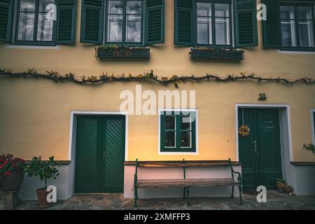 Österreich - 26. Oktober 2023 : Ein gelbes Gebäude mit zwei Fenstern und zwei Türen. Jedes Fenster hat grüne Fensterläden und jede Tür hat einen grünen Rahmen. Da Stockfoto