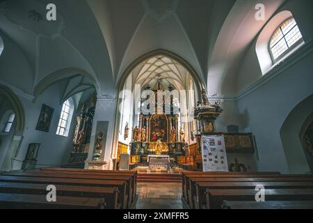 Österreich - 26. Oktober 2023 : das Innere einer Kirche mit hohen Gewölbedecken und Holzbänken. Ein großer Altar mit goldenen Zierleisten und Statuen befindet sich im c Stockfoto