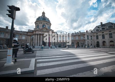 Paris, Frankreich - 19. Oktober 2023 : Ein Polizeibeamter steht neben einem Fußgängerübergang vor einem großen, reich verzierten Gebäude mit Kuppel. Das Gebäude ist direkt am Ort Stockfoto
