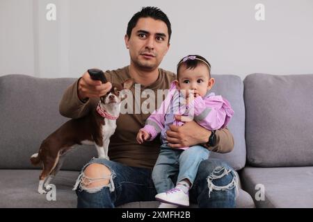 Junger Vater mit Baby in den Armen greift die Fernbedienung Stockfoto