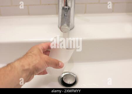 Die Hand eines Mannes gießt Wasser aus einem Wasserhahn. Wasser fließt aus dem Wasserhahn in ein Glas. Stockfoto