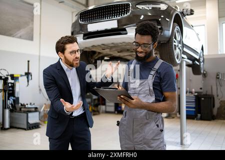 Kunde bespricht Details zur Fahrzeugreparatur mit dem Mechaniker im Service Center Stockfoto