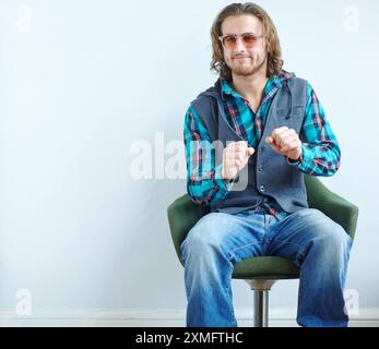 Mode, Sonnenbrille und Mann auf Stuhl an der Wand tanzen zu grooviger Musik, Funk oder Soul auf Mockup Space. Cool, stilvoll und lässig auf Sessel Stockfoto