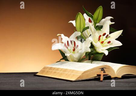 Bibel, Kreuz und Lilien auf grauem Tisch vor braunem Hintergrund, Platz für Text. Religion des Christentums Stockfoto