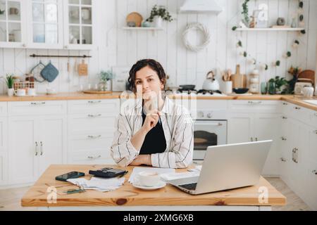 Porträt einer jungen kaukasischen Frau, die zu Hause in der Küche mit Finanzpapieren arbeitet, auf einen Rechner zählt, Rechnungen bezahlt, ein Budget plant Stockfoto