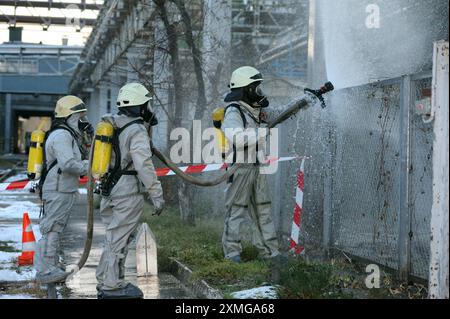 Retter in Schutzgummibezügen, die Pflanzengebiet mit Spritze bewässern. Rettungsmannstraining zur Dekontamination. Stockfoto