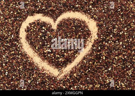 Herz auf verschüttetem Früchtetee gezeichnet, Textur. Blick von oben auf Tee aus Apfel, Zimt, Zitronenschale, Hibiskusblüten, Süßholzwurzel und Nelken. Tee gratis Stockfoto