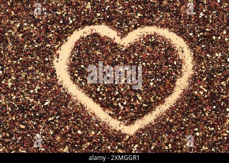 Herz auf verschüttetem Früchtetee gezeichnet, Textur. Blick von oben auf Tee aus Apfel, Zimt, Zitronenschale, Hibiskusblüten, Süßholzwurzel und Nelken. Tee gratis Stockfoto