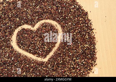 Herz auf verschüttetem Früchtetee gezeichnet, Textur. Blick von oben auf Tee aus Apfel, Zimt, Zitronenschale, Hibiskusblüten, Süßholzwurzel und Nelken. Tee gratis Stockfoto