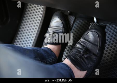 Mann in schwarzen Schuhen, der auf das Pedal der Autobremse drückt, Nahaufnahme Stockfoto