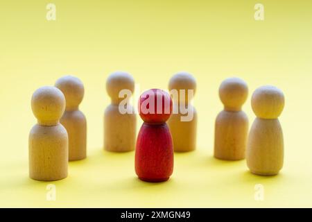 Eine rote Holzfigur umgeben von anderen Holzfiguren, die entweder einen Anführer oder einen diskriminierten Menschen darstellen. Stockfoto