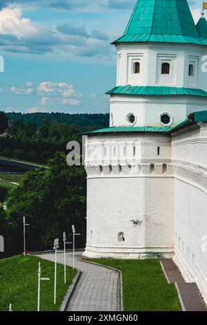 Eine Aufnahme eines historischen Festungsturms aus weißem Stein, gekrönt von einem grünen Dach, auf einem grasbewachsenen Hügel mit einem Weg und umgeben von üppigen grünen Bäumen Stockfoto