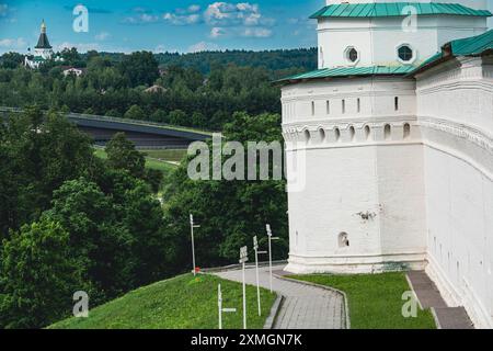 Eine Aufnahme eines historischen Festungsturms aus weißem Stein, gekrönt von einem grünen Dach, auf einem grasbewachsenen Hügel mit einem Weg und umgeben von üppigen grünen Bäumen Stockfoto