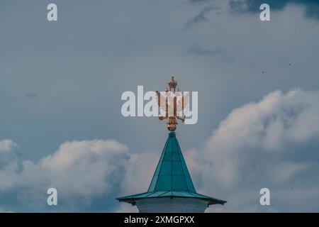 Ein goldener Doppeladler sitzt auf einer türkisfarbenen Kuppel vor dem Hintergrund eines bewölkten Himmels. Der Adler ist ein Symbol des russischen Erbes und fügt einen hinzu Stockfoto