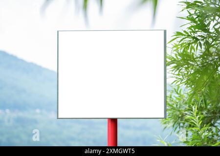 Eine grüne Landschaft mit einem leeren weißen Schild unter blauem Himmel und üppigem Grün im Hintergrund Stockfoto