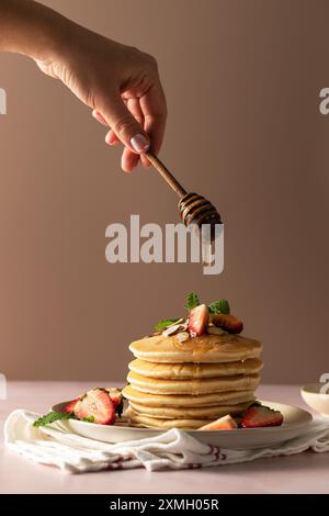 Frau gießt Honig auf Pfannkuchen mit Erdbeeren auf Rosa Stockfoto