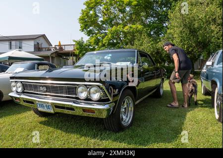 Hilton Beach, Ontario, Kanada - 27. Juli 2024: Black 1966 Chevrolet Chevelle SS auf der Classic Car Show. Mann, der in das Fenster auf der Fahrerseite schaut. Stockfoto