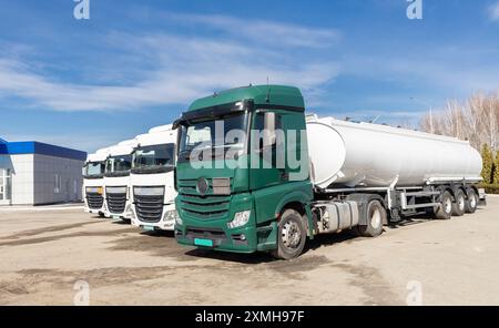 4 LKW-Fahrerhäuser und ein großer Tank, der an sonnigen Tagen nebeneinander geparkt wird. Ansicht der Fahrerhäuser mit Zugmaschine und Anhänger. Nutzfahrzeuge, Werbung für V Stockfoto