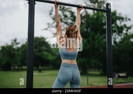 Junge Frau, die im Park Pull-ups macht, um Bizeps, Schultern und laterale Muskeln zu trainieren Stockfoto