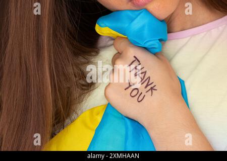 Das Mädchen hält eine ukrainische Flagge in der Hand und auf ihrer Hand steht Dankeschön, Dankbarkeit Stockfoto