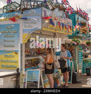 Strandpromenade mit farbenfrohen Meeresfrüchteständen. Ein Mann und eine Frau werden bedient und ein Standhalter beugt sich vor. Flaggen und Hummer Töpfe sind ab Stockfoto