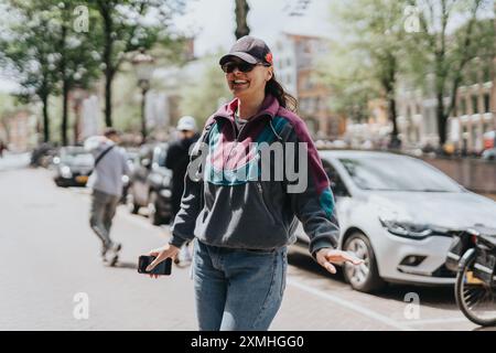 Glückliche Frau in lässigem Outfit, die an einem sonnigen Tag durch die Straßen von Amsterdam spaziert Stockfoto
