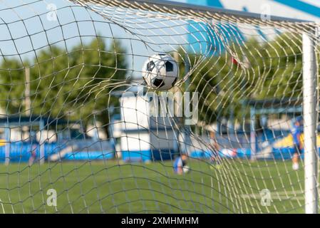 Ein schwarz-weißer Fußball, der durch einen kräftigen Schuss angetrieben wird und das Netz durchbricht, um ein perfektes Tor zu erzielen. Das wulstige Netz betont den Aufprall und die Qualität Stockfoto