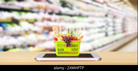 Frisches Essen und Gemüse im Warenkorb auf dem mobilen Smartphone auf Holztisch mit verschwommenem Hintergrund Supermarkt Gang Online-Konzept Stockfoto