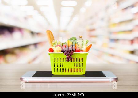 Frisches Essen und Gemüse im Warenkorb auf dem mobilen Smartphone auf Holztisch mit verschwommenem Hintergrund Supermarkt Gang Online-Konzept Stockfoto