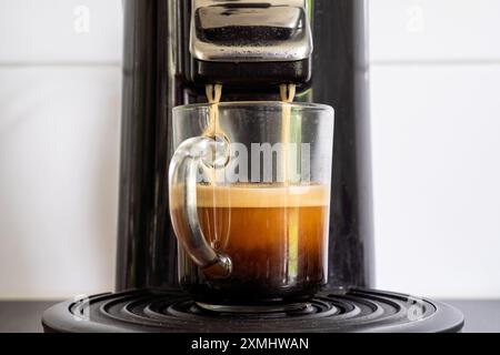 Glasbecher mit frisch gebrühtem Kaffee aus der Kaffeepadmaschine Stockfoto