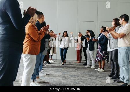 Eine vielfältige Gruppe von Geschäftsleuten, die eine Frau in einem Unternehmensumfeld applaudieren und feiern und dabei Teamarbeit, Leistung und Inklusivität widerspiegeln Stockfoto