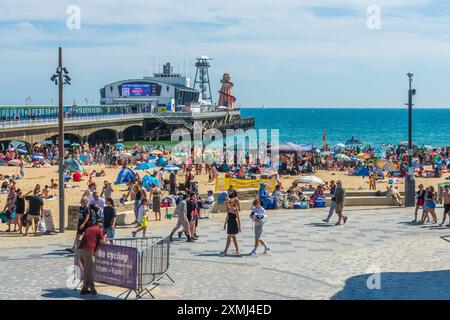 Bournemouth, Großbritannien - 28. Juli 2024: Menschen auf der Promenade vor dem Bournemouth Pier und eine Menschenmenge am Strand genießen das heiße Wetter. Stockfoto