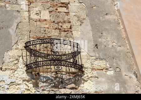 Rustikaler Balkon mit kunstvollem Geländer an einer verwitterten Steinmauer. Stockfoto