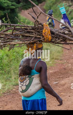 FORT PORTAL, UGANDA - 12. MÄRZ 2020: Eine einheimische Frau mit Feuerholz und ihrem Baby in der Kraterseen-Region nahe Fort Portal, Uganda Stockfoto