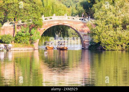 Boote, die unter einer Mondbrücke im Quyuan-Garten am Westsee in Hangzhou, China, vorbeifahren Stockfoto