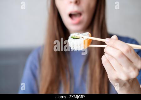 Eine junge Frau mit langen Haaren hält Rollen auf Stöcken vor dem Hintergrund eines offenen Mundes, Nahaufnahme Stockfoto