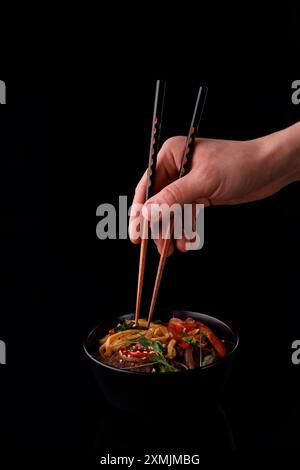 Brate Nudeln mit Gemüse und Garnelen in schwarzer Schüssel rühren. Hintergrund aus Schiefer. Draufsicht. Kopierbereich. Stockfoto