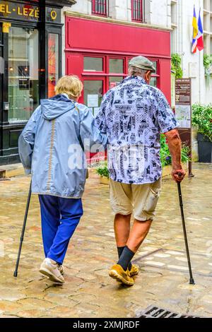 Älteres Paar mit Wanderstöcken, Arm in Arm im Stadtzentrum - Loches, Indre-et-Loire (37), Frankreich. Stockfoto