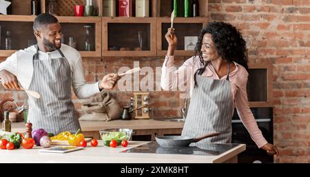 Lustiges Ehepaar kämpfen mit Utensilien Werkzeuge in der Küche Stockfoto