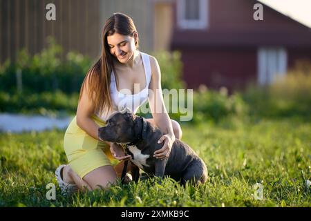 Außenporträt einer jungen Europäerin mit ihrem amerikanischen Tyrannehund am Sommerabend im Dorf. Stockfoto