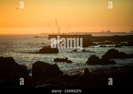Die Küste von Matosinhos mit der Silhouette des Hafens und Felsen im Hintergrund bei einem atemberaubenden Sonnenuntergang in Portugal. Stockfoto
