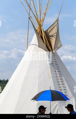 Zwei Ureinwohner unter einem blauen Regenschirm, neben einem Tipi oder Tipi im Tsuut'ina Rodeo und Powwow. Alberta Kanada Stockfoto