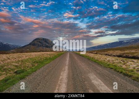 Die Gravel Road führt zum abgerundeten Berg unter dem lebendigen Himmel in Island Stockfoto