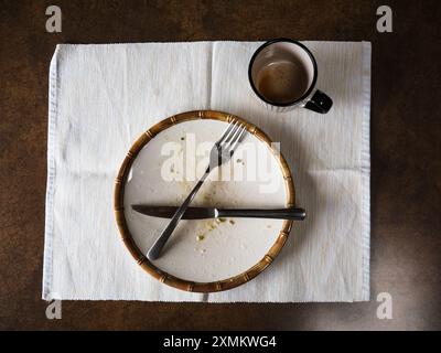 Leeren Sie Frühstücksteller, Gabel, Messer und leere Kaffeetasse auf einer einzelnen Tischdecke Stockfoto