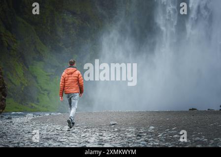 Person in Orange Jacke, die zum majestätischen Skogafoss Wasserfall in Island geht Stockfoto