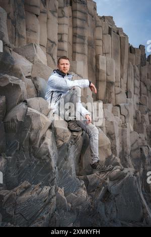 Person, die auf Basalt Säulen am Reynisfjara Beach in Island sitzt Stockfoto