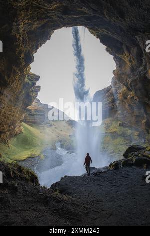Silhouettenfigur hinter dem Seljalandsfoss-Wasserfall in Islands üppiger Landschaft Stockfoto