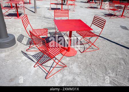 Roter Tisch und Stühle im Café-Stil mit langen Schatten in der Nachmittagssonne auf einem platz im Freien Stockfoto