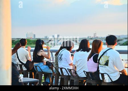 Taiwan - 28. Juli 2024: Touristen genießen Bier und genießen einen atemberaubenden Sonnenuntergang am Dadaocheng Pier Plaza, einem lebhaften Flussufer in Taipeh. Stockfoto