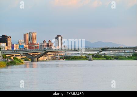 Blick vom Dadaocheng Pier Plaza in Richtung Zhongxiao Bridge, mit Blick auf den Tamsui Fluss, entfernte Berge und eine Mischung aus Taipeis modernen Wolkenkratzern. Stockfoto